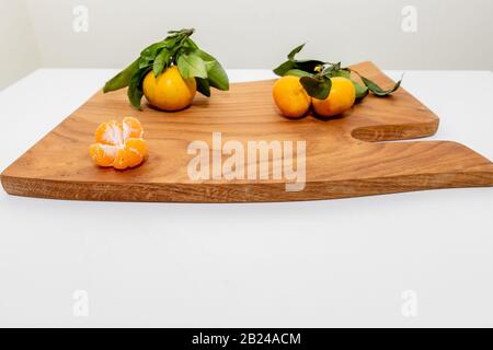 Frische, saftige Clementine-Mandarinen, Winterfrüchte.Halbgeschälte Mandarine und Schale auf einer Holzoberfläche, minimalistisches Stillleben. Mandarine oder Stockfoto