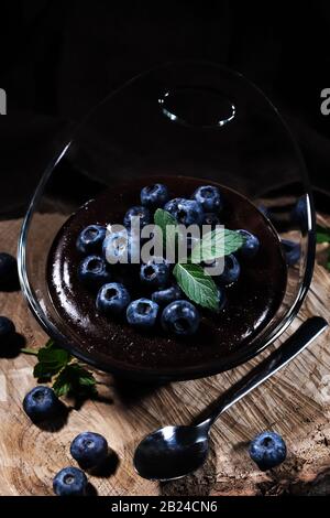 Schokoladenpudding mit Blaubeeren, schön in einer Glasschale auf einem Holzteller angeordnet Stockfoto