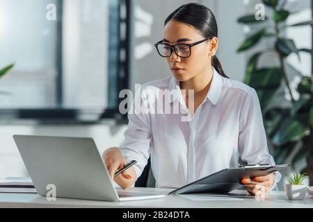 Asiatischer Übersetzer in Brillen, die online mit Laptop im Büro arbeiten Stockfoto