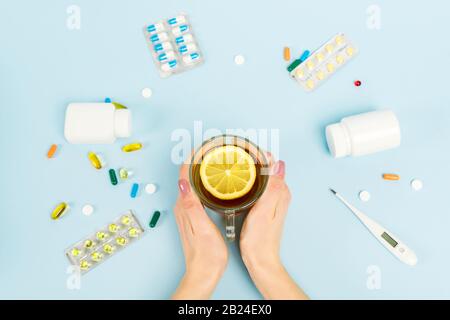 Draufsicht über die Frau, die eine Tasse Tee mit geschnittener Zitrone in der Nähe von Pillen und Digitalthermometer in Blau hält Stockfoto