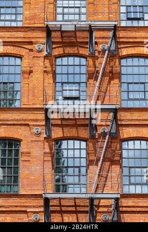 Klassische Industriebaufassade aus rotem Backstein mit Feuerlöschleitertreppen Stockfoto