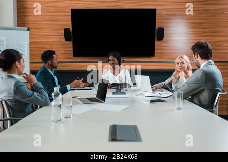 Junge multikulturelle Geschäftsleute, die während des Treffens im Konferenzsaal mit lcd-Bildschirm an der Wand sprechen Stockfoto