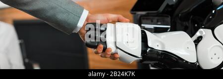 Teilweiser Blick auf Unternehmer und Roboter, der die Hände im Büro schüttelt, Panoramaaufnahme Stockfoto