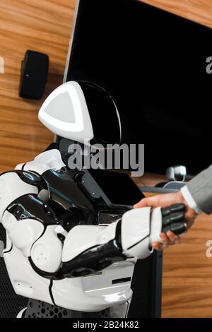 Teilansicht des Geschäftsmannes, der mit humanoidem Roboter im Büro die Hände schüttelt Stockfoto