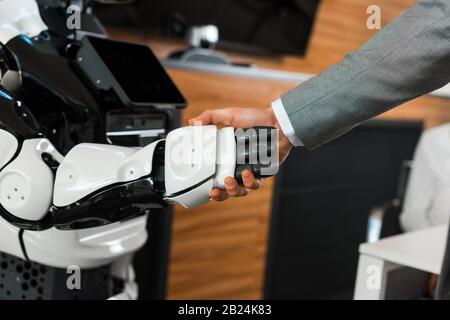 Teilansicht des Geschäftsmannes, der mit humanoidem Roboter im Büro die Hände schüttelt Stockfoto