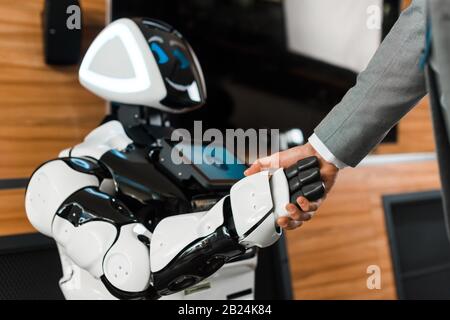 Beschnittenes Bild von Geschäftsleuten, die mit lächelndem Roboter im Büro die Hände schütteln Stockfoto