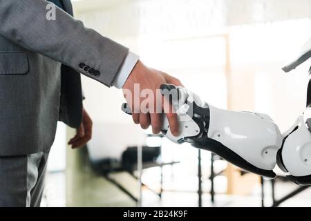 Beschnittenes Bild von Geschäftsleuten und Robotern, die die Hände im Büro schütteln Stockfoto