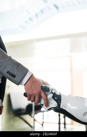 Teilansicht des Geschäftsmannes und des Roboters, der die Hände im Büro schüttelt Stockfoto