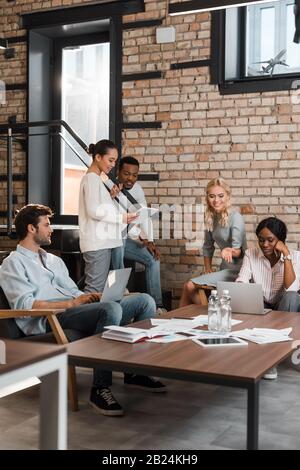 Junge multikulturelle Geschäftsleute mit Geräten, die Brainstorming im Büro haben Stockfoto