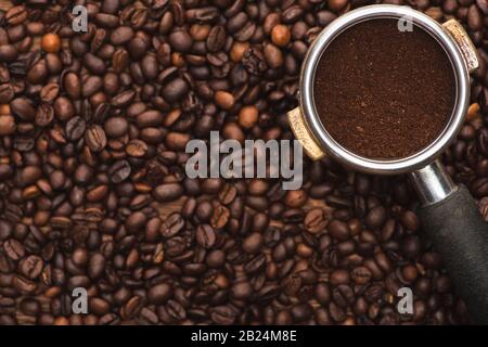 Draufsicht über gemahlenen Kaffee im Filterhalter auf frisch gerösteten Kaffeebohnen Stockfoto