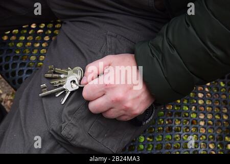 Der Mann sitzt auf einer Metallbank und hält Schlüssel in der Hand. Stockfoto