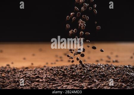 Gebratene Kaffeebohnen fallen auf schwarzem Grund auf den Haufen Stockfoto