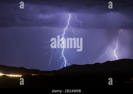 Nachthimmel mit einem gegabelten Blitzschlag, der bei einem Gewitter in der Nähe von Phoenix, Arizona, einen Berg trifft Stockfoto