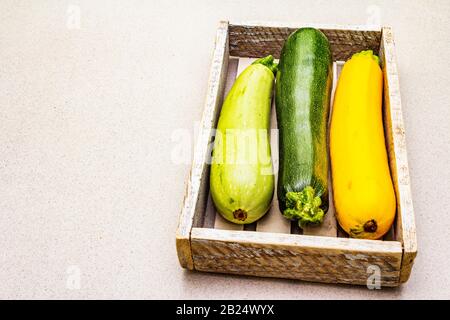 Verschiedene bunte Zucchini in Holzkiste. Frisches Gemüse zum Kochen. Ernte auf Steinhintergrund, Kopierraum Stockfoto