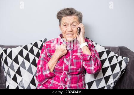 Thema alte Person verwendet die Technologie. Reifen glücklich Freude Lächeln aktiv graue Haare Kaukasischen falten Frau nach Hause sitzen im Wohnzimmer auf dem Sofa und mit einem Stockfoto