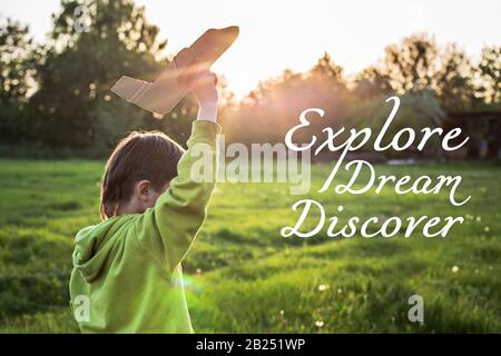 Text Entdecken Sie den Traum. Der Junge in einer grünen Jacke läuft bei Sonnenuntergang über das Feld. Das Kind startet ein Papierflugzeug. Glückliche Kindheit. Gehen auf t Stockfoto