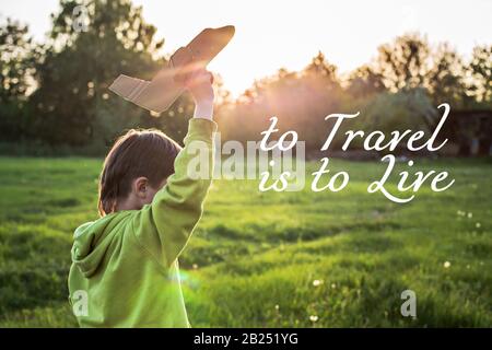 Der Text, Der Zu reisen ist, soll leben. Kind startet Papierflugzeug. Junge in grüner Jacke läuft bei Sonnenuntergang über das Feld. Glückliche Kindheit. Gehen Sie mit auf die Straße Stockfoto