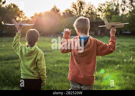 Kind startet Papierflieger. Junge, grüne Jacke über Feld bei Sonnenuntergang läuft. Glückliche Kindheit. Zu Fuß auf der Straße ohne ein Telefon. Stockfoto