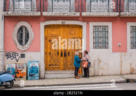 Zwei alte portugiesische Frauen plaudern auf der Straße vor einem alten rosafarbenen Gebäude in Lissabon Portugal Stockfoto