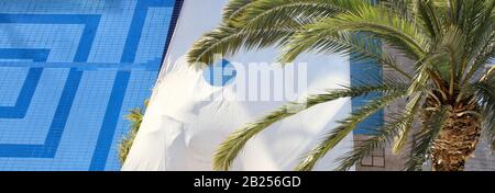 Ein computergroßes Banner zeigt einen Blick von oben auf einen Swimmingpool mit weißem Sonnenschutz und einem Teil einer Palme. Stockfoto