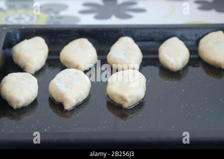 Pasteten auf einem Backblech, das zum Backen bereit ist. Der buschförmige Teig liegt auf einem schwarzen Backblech. Hausbackvorgang. Stockfoto