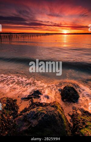 Satte Farben von Orange und Rot am Himmel über einem Poole Harbour Jetty in der Nähe von Sandbanks Stockfoto