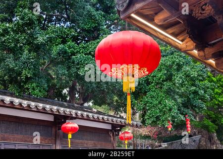 Schöne rote chinesische Laterne, die an Traufen des traditionellen chinesischen alten chinesischen Holzgebäudes hängt, um den chinesischen Festtag in einem zu schmücken Stockfoto