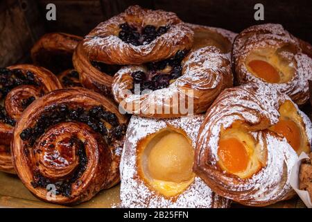 Frisch gebackene dänische Gebäckstücke, Puder, Aprikosen, Blaubeeren, Rosinen, Zimtschwirl in Puderzucker und Glasur verstaubt Stockfoto