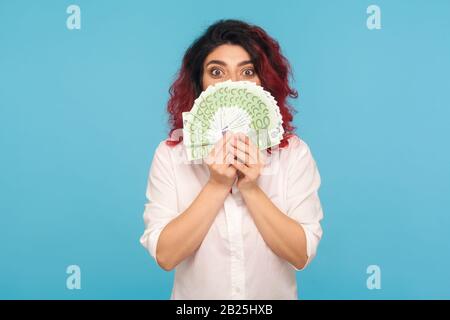 Porträt der überraschten Unternehmerin, die sich hinter Geld versteckt, ihr Gesicht mit Euro-Banknoten bedeckt und mit großen überraschten Augen aussieht, schockiert expre Stockfoto
