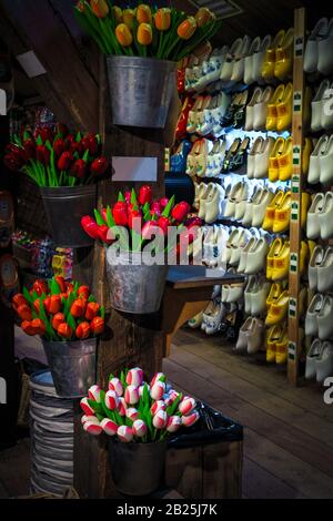 Zauberhafte bunte Blumensträuße aus Holztulpen im Metalleimer und Holzschuhe in einer Reihe an der Wand. Traditioneller Souvenirladen mit Handma Stockfoto