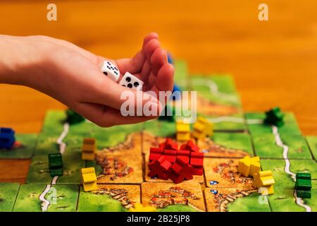 Hand wirft die Würfel auf den Hintergrund farbenfroher, verschwommener Fantasy-Board-Spiele, Spielmomente in Dynamik. Ausgewählter Fokus. Stockfoto
