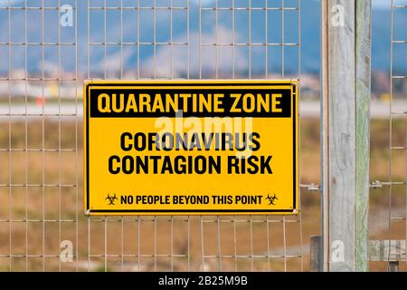 Coronavirus Konzept: Ein schwarz-gelbes Schild, das an einem Metallzaun hängt und eine Warnung anzeigt, den Quarantänebereich nicht zu überschreiten Stockfoto