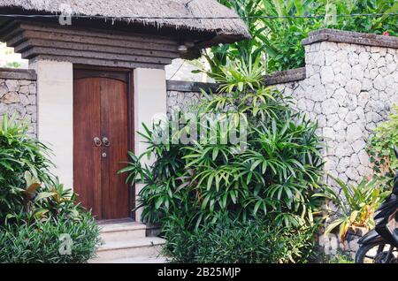 Blick auf die Haustür in einem von grünen Pflanzen umgebenen Steinzaun. Wohnvilla in den Tropen. Bali, Indonesien Stockfoto