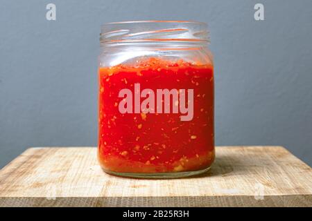 Glas mit Sauce Adjika aus Tomaten, Chili und süßen Paprika auf einem Holztisch grauer Hintergrund. Stockfoto