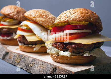 Leckere hausgemachte Burger auf einem Holzständer mit grauer Hintergrundansicht. Stockfoto