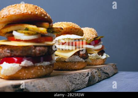 Drei Burger auf einem Holzwald stehen auf grauem Grund. Herzhaftes Mittagessen.Nahaufnahme. Stockfoto