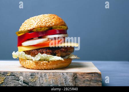 Saftiger Burger mit Häckchen, Käse und Gemüse auf grauem Grund mit Kopierraum. Doppel-Cheesebburger auf Holzplatten. Stockfoto