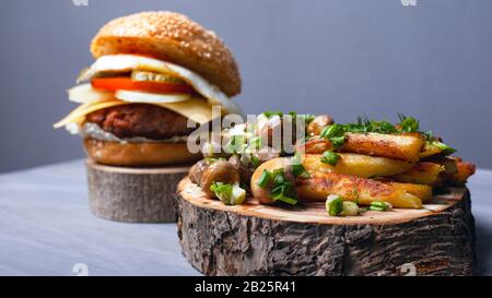 Gebratene Kartoffeln mit Pilzen und ein saftiger Burger auf Holzbrettern. Home fast Food. Stockfoto