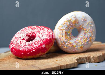 Süße mehrfarbige, verschiedene Donuts mit Puder und Puder auf einem Holzbrett auf grauem Hintergrund. Stockfoto