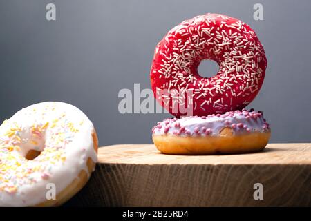 Mehrfarbige Weihnachts-Donuts auf einem Holzständer auf grauem Grund gepudert. Glasur in rot-weißer und violetter Farbe. Stockfoto