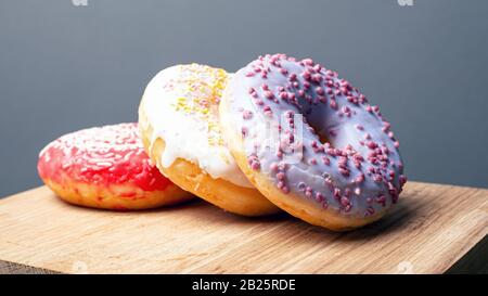 Lecker Donuts mit mehrfarbigem Glasur in rot-weißer und violetter Farbe mit Pulver auf einem Holzbrett auf grauem Grund. Weihnachtsessen. Nahaufnahme. Stockfoto