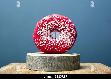 Donut mit roter Glasur und weißem Pulver auf einem Holzständer auf grauem Grund. Süßer Bun auf einem dekorativen Waldständer. Stockfoto