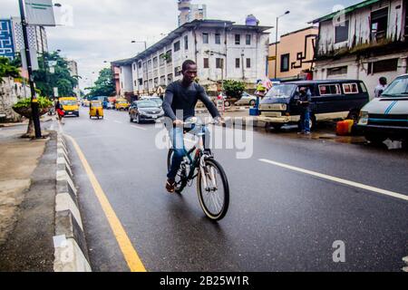 Ein Mann, der auf einer Straße in Lagos, Nigeria, mit dem Fahrrad unterwegs ist. Stockfoto