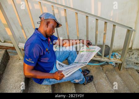 Ein Mann liest Zeitung auf einer Straße in Lagos, Nigeria. Stockfoto