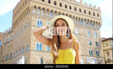 Porträt eines hübschen lächelnden Touristenmädchens in Florenz mit Palazzo Vecchio Palast auf dem Hintergrund. Hübsche junge Frau mit gelbem Kleid im Urlaub Stockfoto