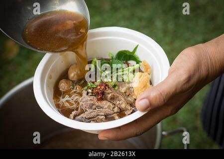 Suppe mit einer Pfanne in einer Schüssel mit thailändischer Nudelsuppe aus Rindfleisch gießen Stockfoto