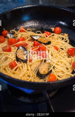 Nahaufnahme von Spaghetti Vongole mit roma-tomaten und Muscheln, die in einer Pfanne auf einem Gasherd erhitzt werden Stockfoto