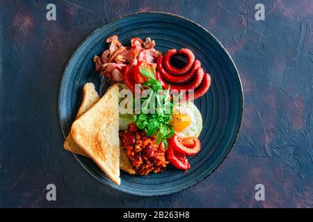 Draufsicht auf gebratenes Ei, Wurst, Speck, Gemüse und Toastbrot Stockfoto