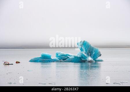 Joekulsarlon Glacier Lagoon tiefes blaues Eis mit Schichten vulkanischer Asche neben Motorbooten Stockfoto