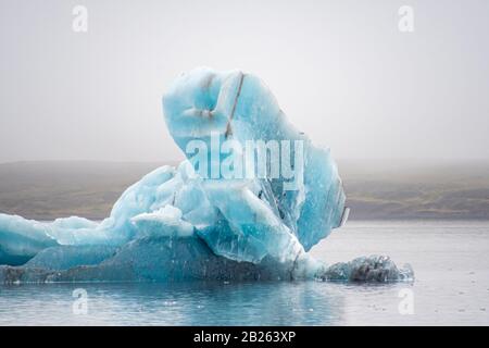 Joekulsarlon Glacier Lagoon tiefblauer Eisberg mit einigen dunklen Schichten vulkanischer Asche Stockfoto